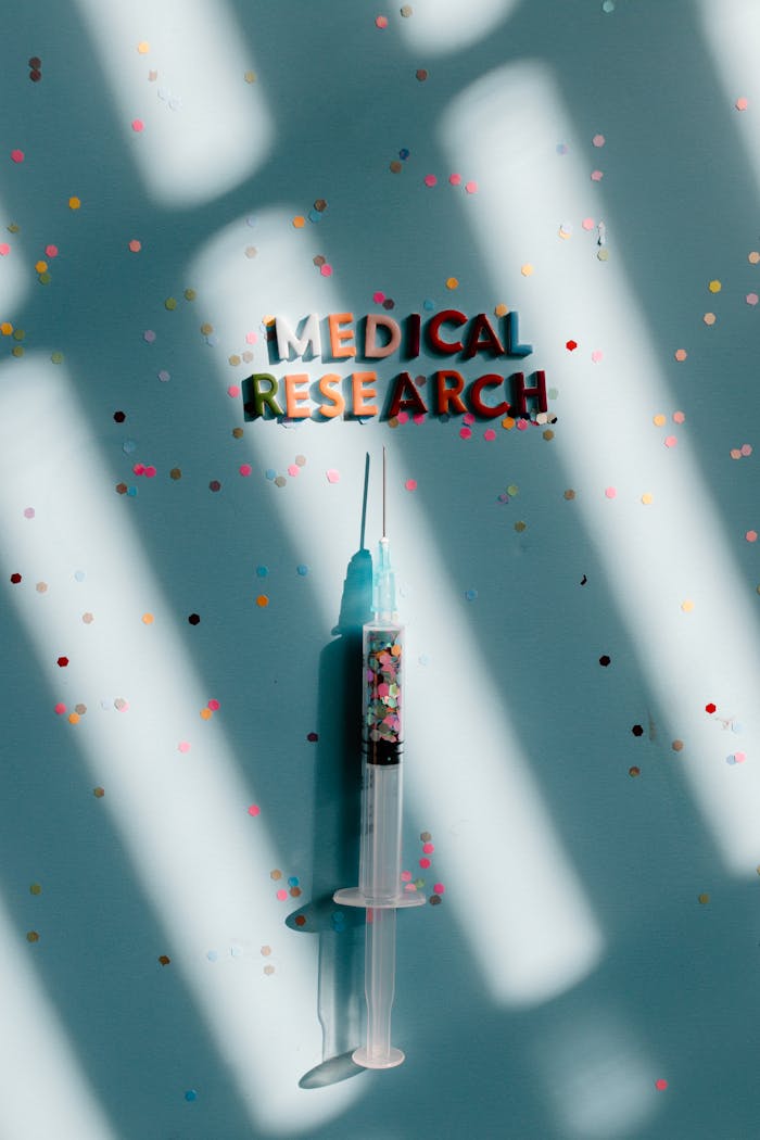 Syringe on a blue background with colorful confetti, symbolizing medical research.